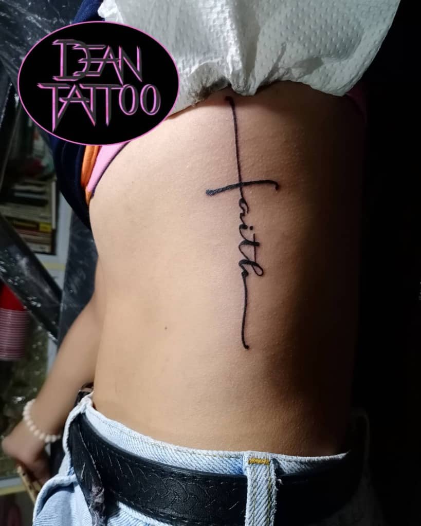 A side tattoo elegantly transforms the word "faith" into a cross, gracefully etched on the person's torso
