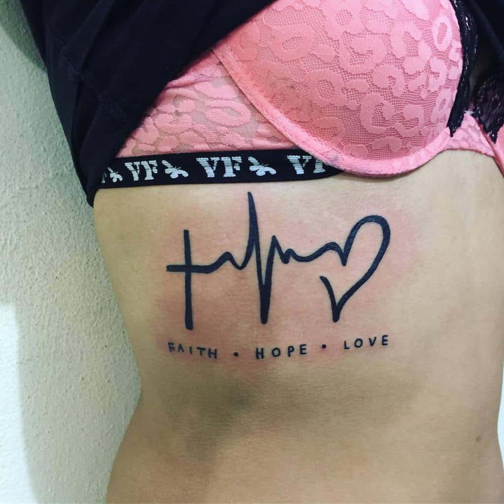 Tattoo of a cross, heartbeat, and heart on a woman's side with the words "Faith Hope Love" elegantly scripted below it