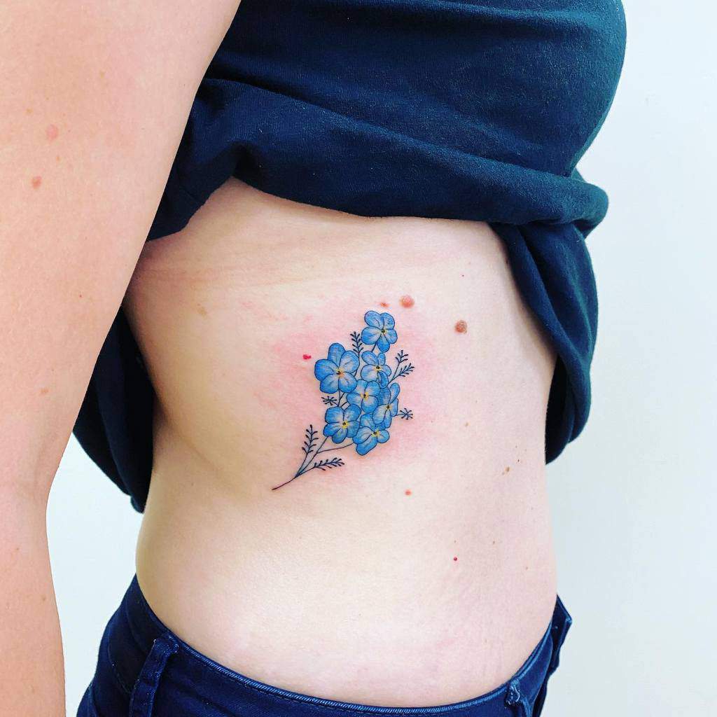 A delicate cluster of forget-me-not flowers tattooed along the side, with soft blue petals and fine, detailed stems