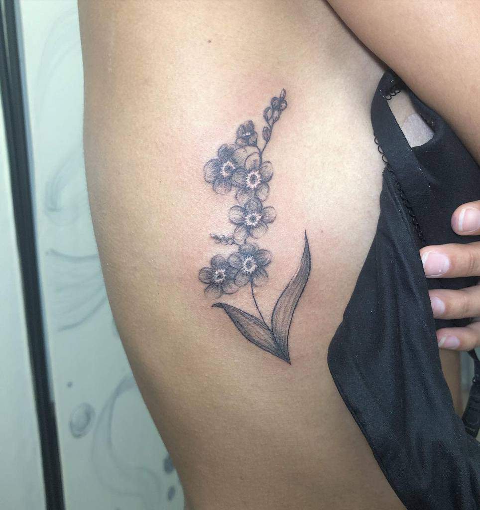 A stunning black and gray floral tattoo, featuring delicate forget-me-nots, graces the woman's side