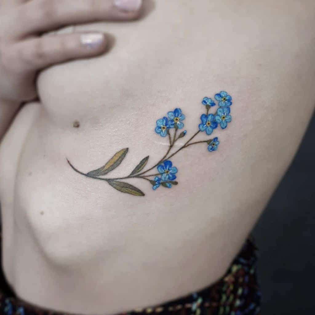 Close-up of a floral tattoo featuring delicate blue forget-me-nots on a woman's side