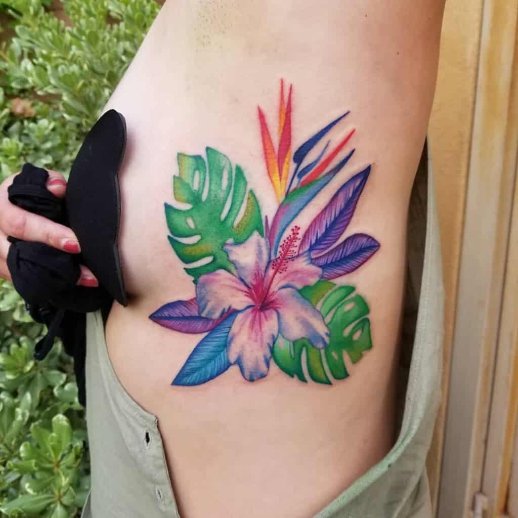 Colorful tropical flower tattoo with leaves on a side