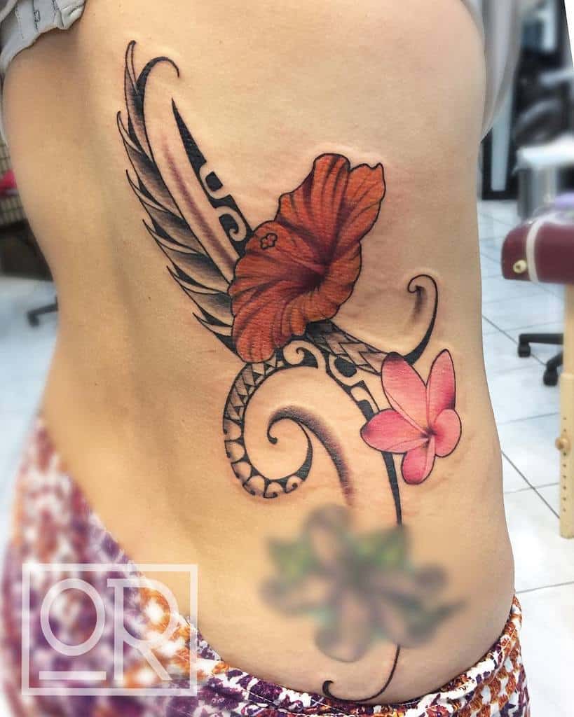 Side tattoo featuring a bold red hibiscus flower and pink plumeria, combined with black tribal patterns and flowing lines