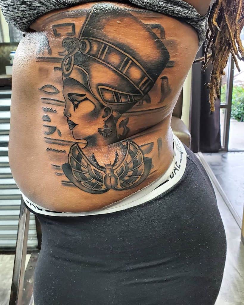 Tattoo of Nefertiti as an Egyptian queen with hieroglyphs and a scarab on a woman's side torso
