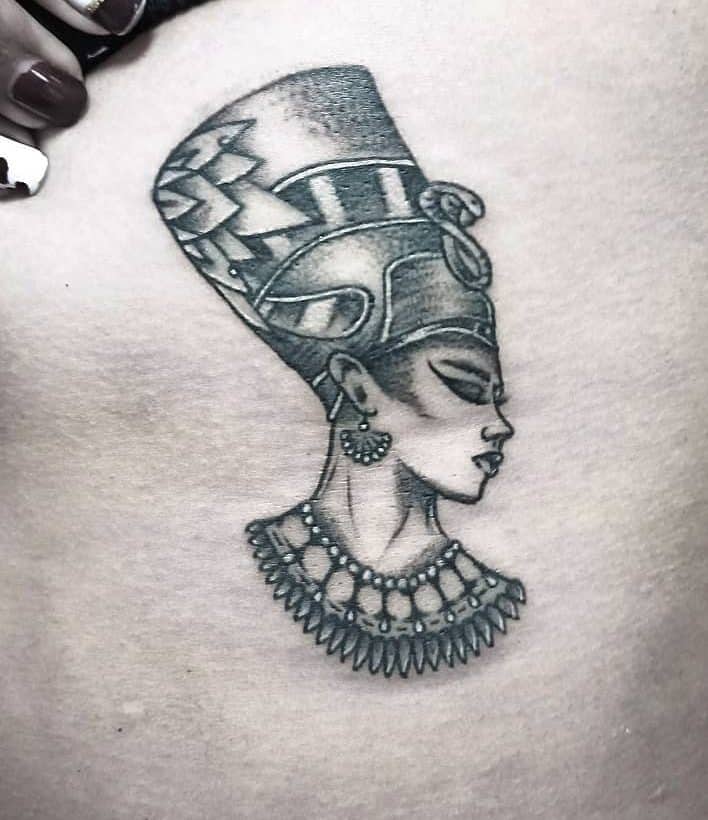 Tattoo of an Egyptian queen with a tall headdress and detailed necklace in black and gray ink