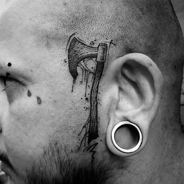 Black and grey hatchet tattoo on the side of the head, featuring a dripping ink effect and fine detailing for a bold and edgy design.