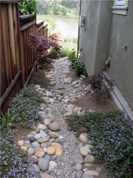 Narrow garden path with stones, plants, and wooden fence