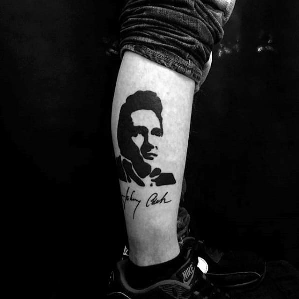 Minimalist black ink tattoo of Johnny Cash's portrait with his signature below, capturing the iconic musician's timeless legacy on the leg