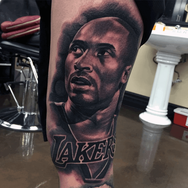 A striking black and white tattoo of Kobe Bryant, showcasing his focused expression, with the "LAKERS" text prominently displayed below his face.