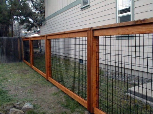 A wooden and wire fence lines the house, neatly dividing the grassy yard space