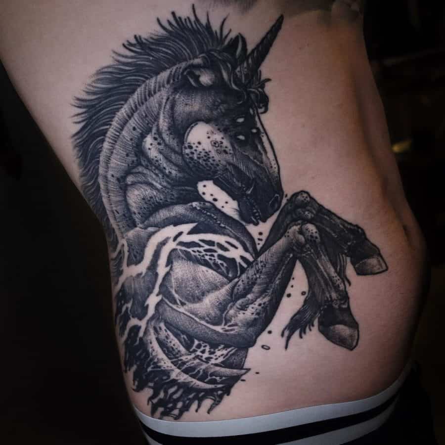 Dark and bold black ink tattoo of a rearing unicorn with a muscular body, intense shading, and water elements blending into its form.
