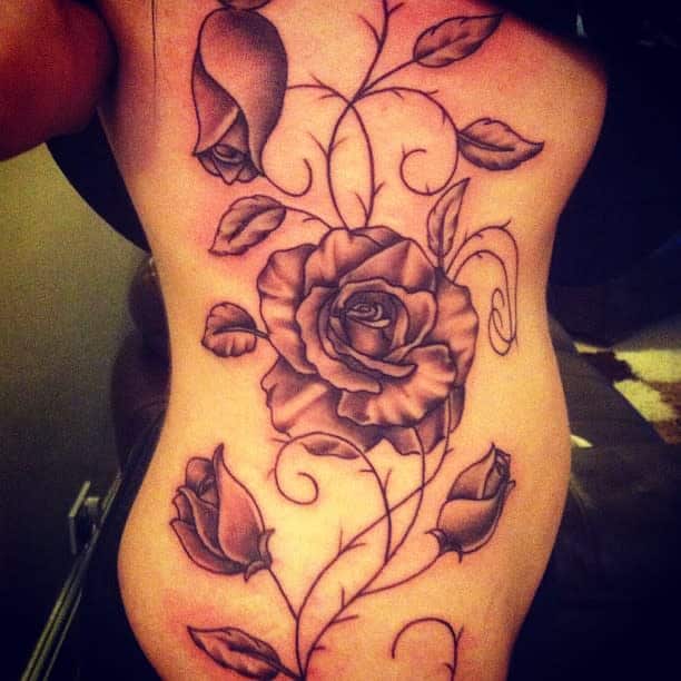 Elegant rose vine tattoo along the side of the body, featuring blooming roses, buds, and delicate swirling vines with detailed shading