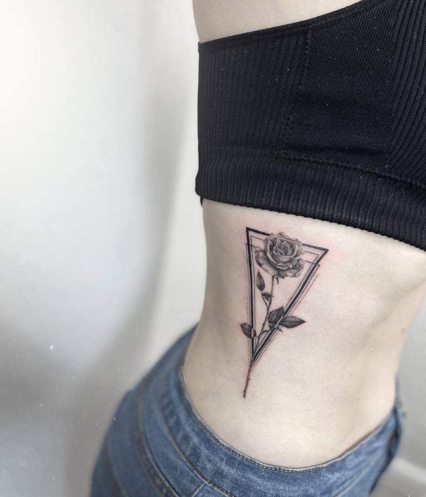 A rose tattoo with a delicate stem gracefully weaves within a triangle on a woman's side