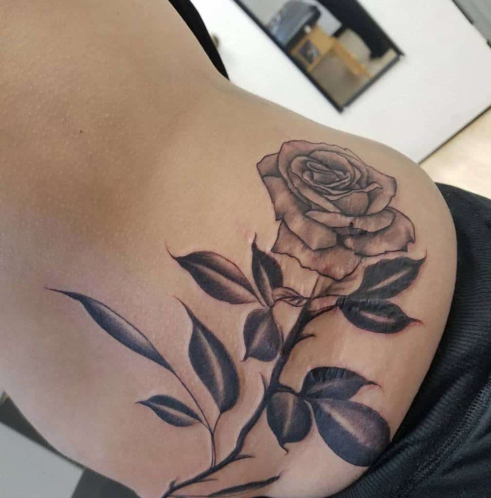 Elegant black and gray rose tattoo with detailed leaves and stem, beautifully placed on the side of the body