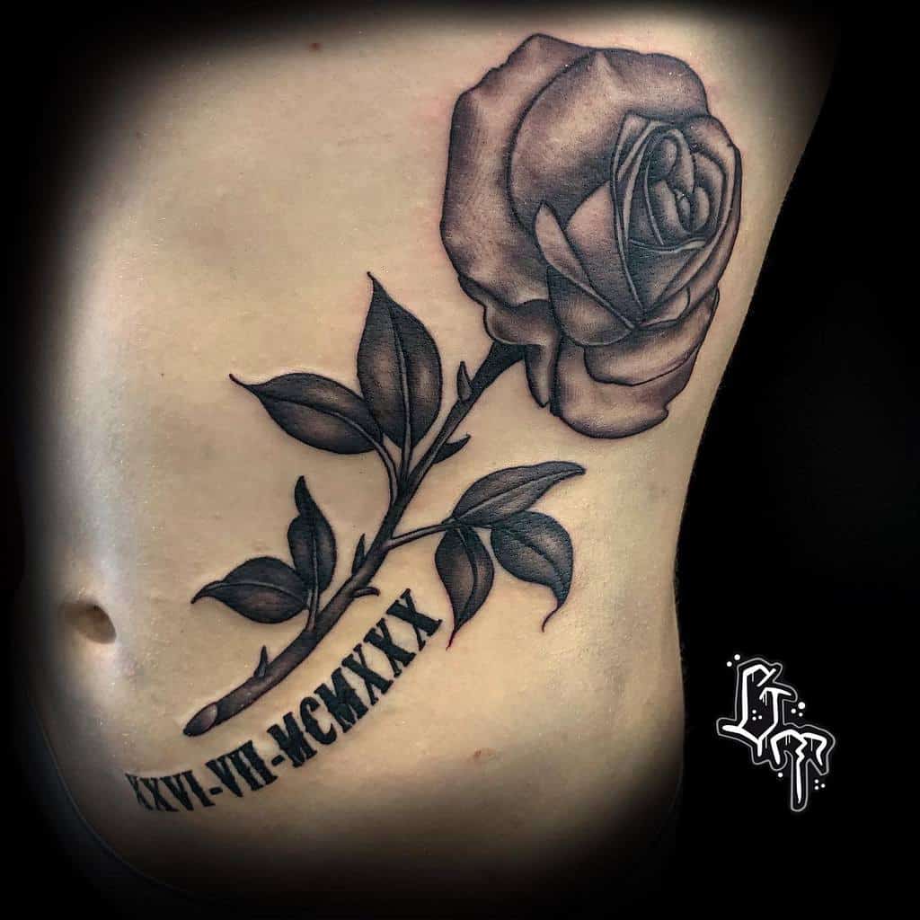 Tattoo of a rose with leaves and a graceful stem, accompanied by Roman numerals, elegantly inked on a side torso