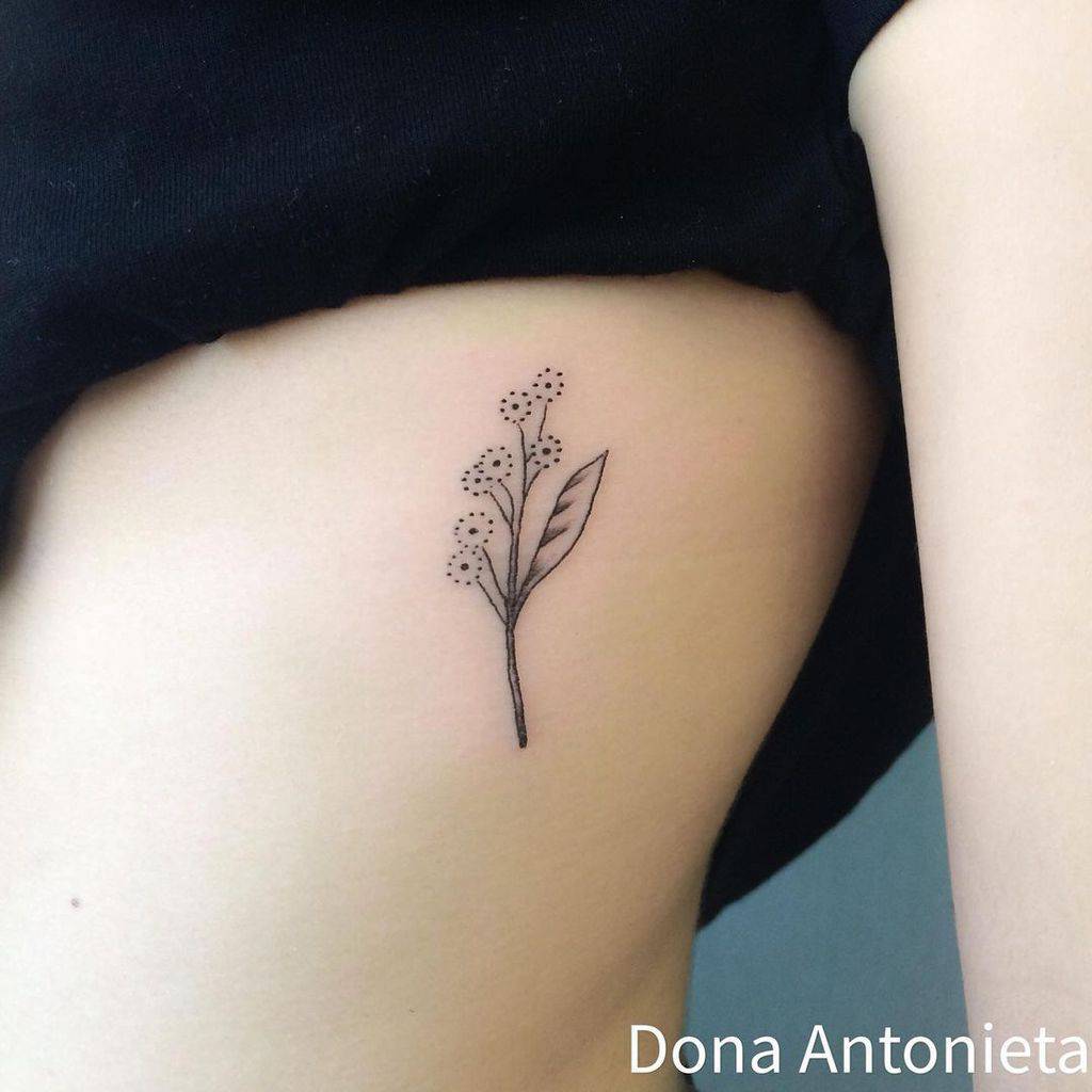 Simple floral tattoo on side torso, featuring a delicate branch with small flowers and a leaf