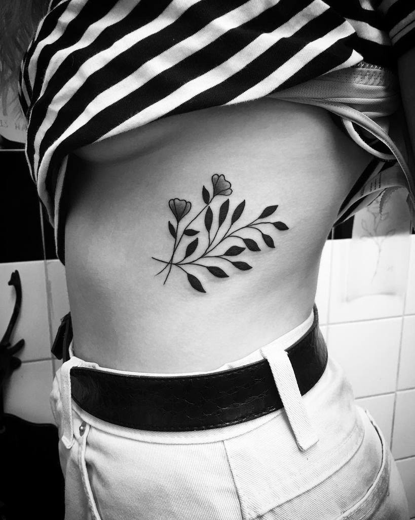 Black and white tattoo of a floral design on a woman's side