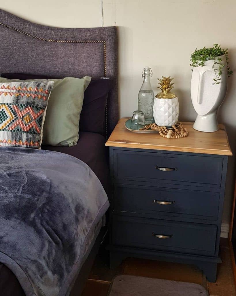 Blue bedside table with decorative pineapple, plant vase, and water bottle.