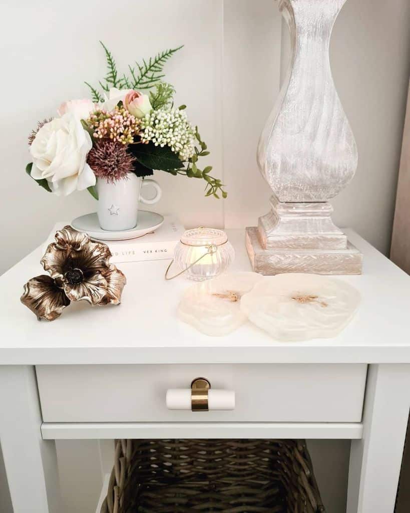 White bedside table with floral arrangement, candle, and decorative lamp.