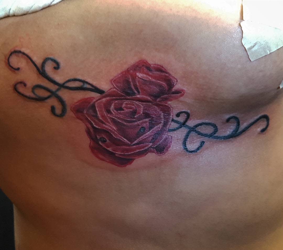 A red rose tattoo with black swirling vines on skin