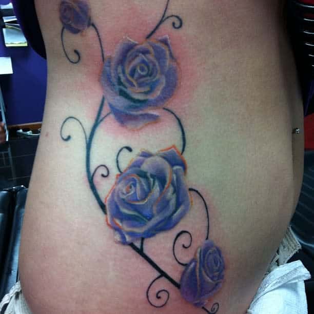 Tattoo of purple roses with swirling vines on a woman's side