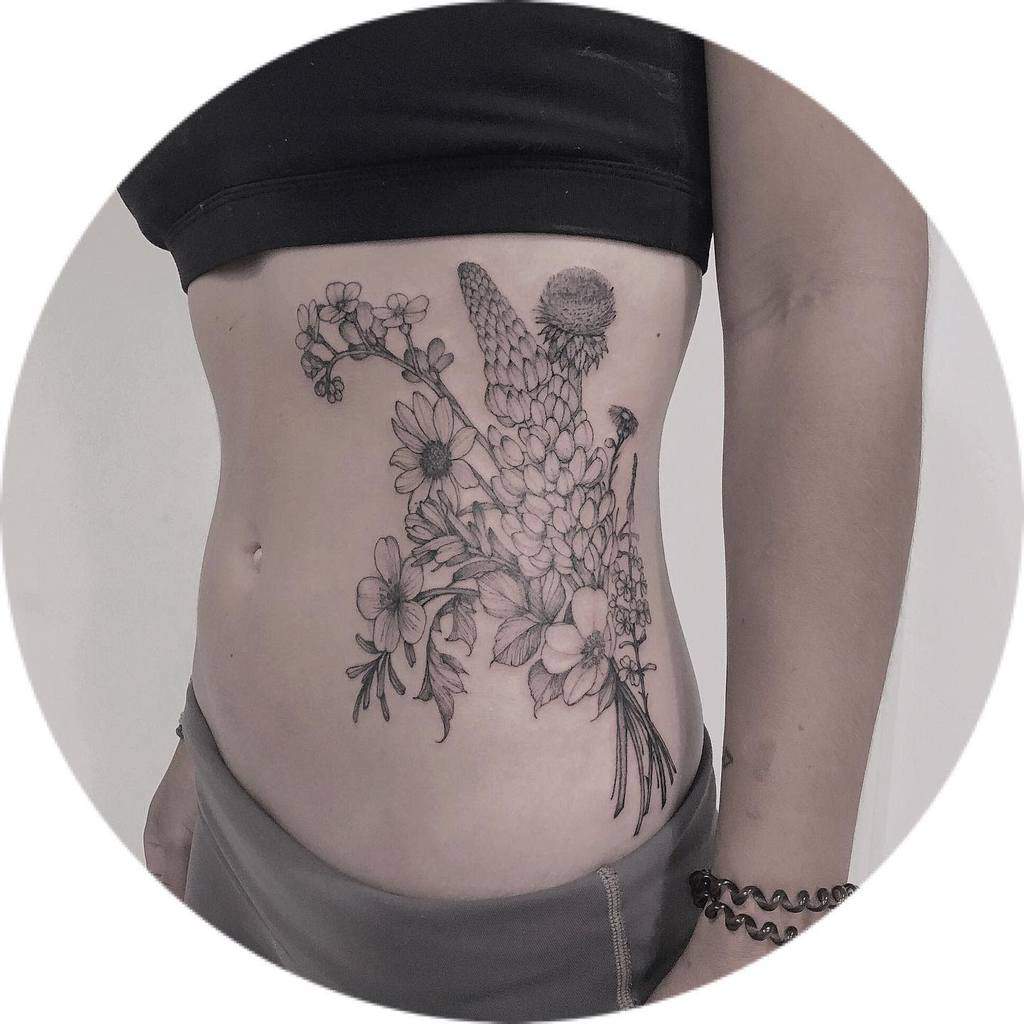 Elegant side tattoo featuring a detailed bouquet of wildflowers, including daisies and lupines, in fine black ink