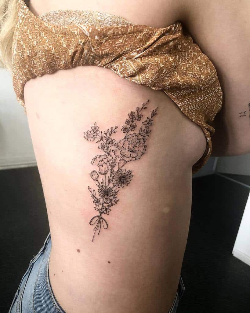 Delicate side tattoo featuring a tied bouquet of wildflowers with intricate black ink linework and fine details