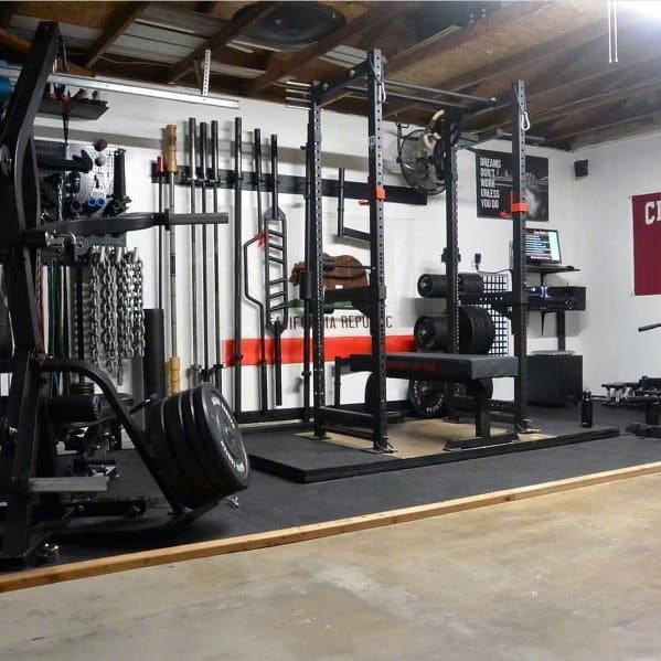 Garage gym with black walls, squat rack, dumbbells, weight plates, and cardio equipment.