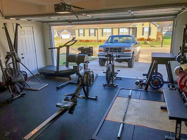 Garage gym with lifting platform, treadmill, rower, air bike, and GHD machine in an open setup.