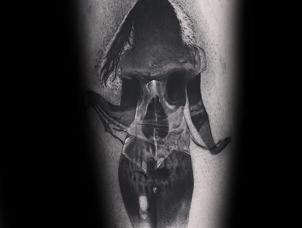 Black and grey surrealist tattoo of a woman with a skull blended into her torso, creating a striking double-exposure effect with realistic shading.