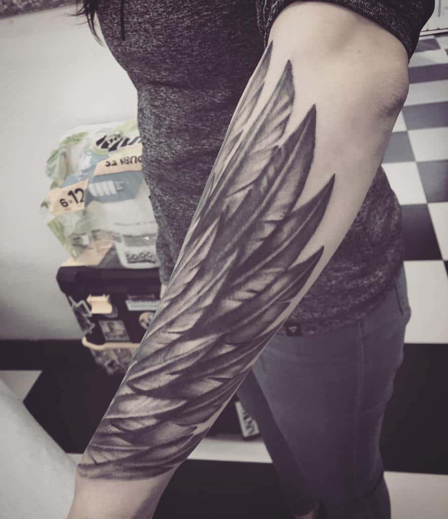 A detailed black angel wings feather tattoo with intricate shadings