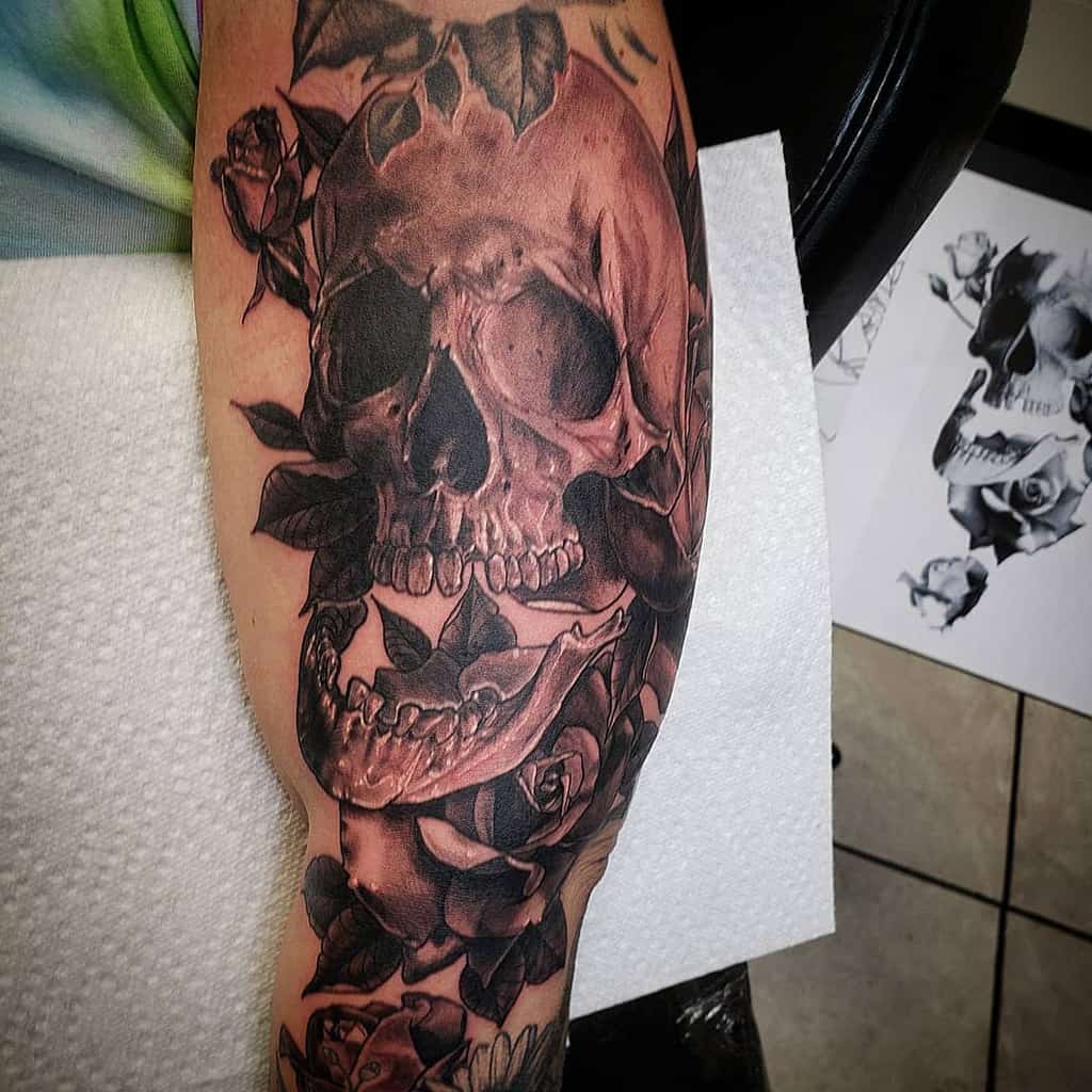 Black and grey tattoo sleeve of a realistic skull surrounded by roses, featuring intricate shading and high-detail linework for a dramatic effect.