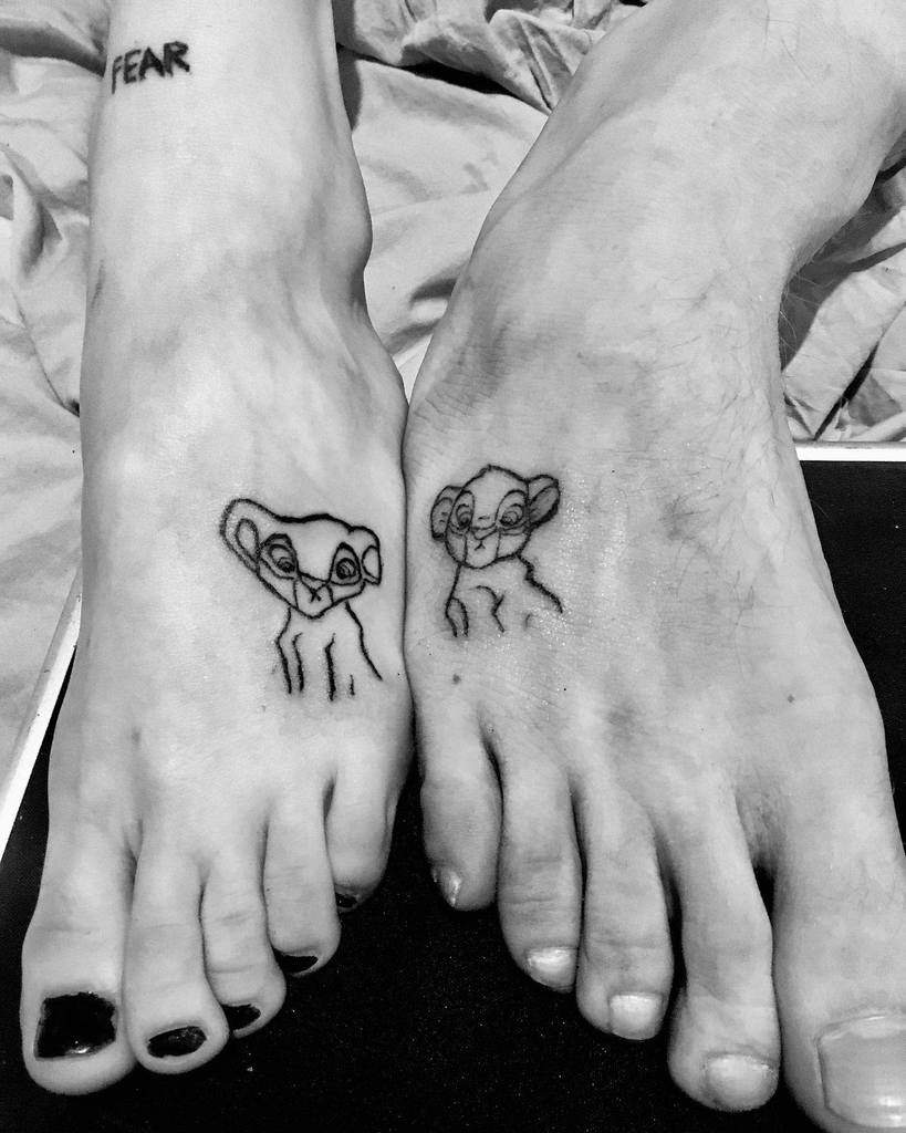 Black and white image of two feet with Nala and Simba as cubs and the word "FEAR" tattooed on an ankle
