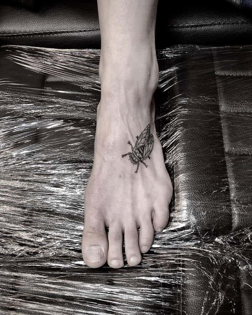 Minimalist foot tattoo of a detailed cicada in black ink, showcasing fine linework and symmetry