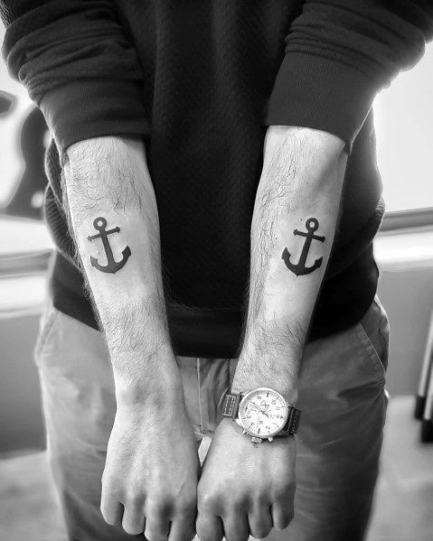 Matching black anchor tattoos on both forearms, featuring a bold and simple design, symbolizing stability, strength, and a nautical connection.