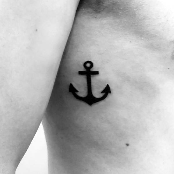 Small black anchor tattoo on the ribcage with a bold, simple design, symbolizing strength, stability, and a deep connection to the sea.