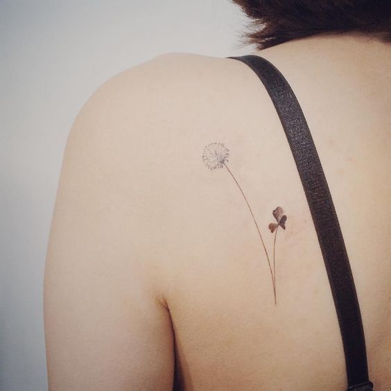 Minimalist dandelion and clover tattoo on the upper back, symbolizing luck, wishes, and the beauty of simplicity.
