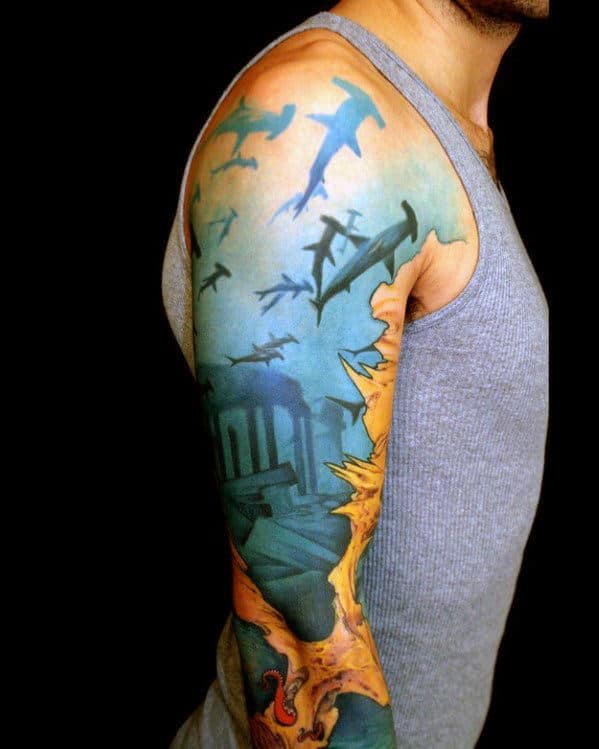 Person with a sleeve tattoo featuring sharks, underwater scene, and a dragon