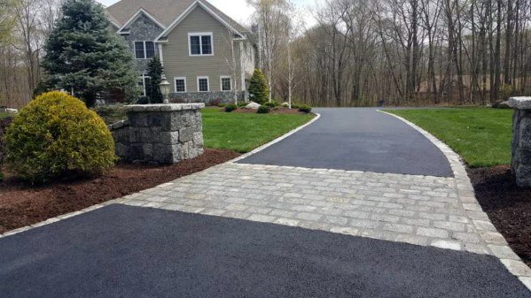 Asphalt driveway with stone edging and a decorative stone entrance near a landscaped yard.