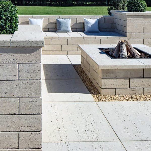 Outdoor stone patio with a cozy fire pit, cushioned seating, and lush greenery in the background