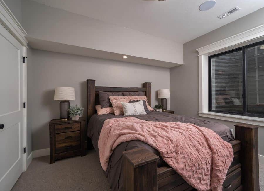 Cozy basement bedroom with wooden bed frame, soft pink bedding, and natural light from a large window.
