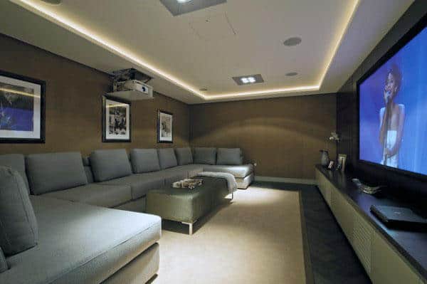 Home theater room with large gray sectional sofa, projector, framed photos, and a woman singing on a big screen