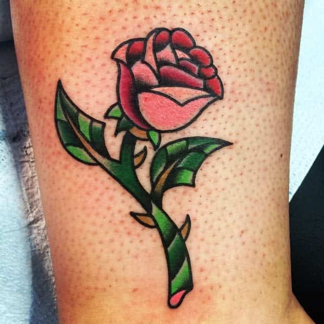 A simple, colorful tattoo of the Beauty and the Beast rose, featuring vibrant pink petals and green leaves with bold outlines