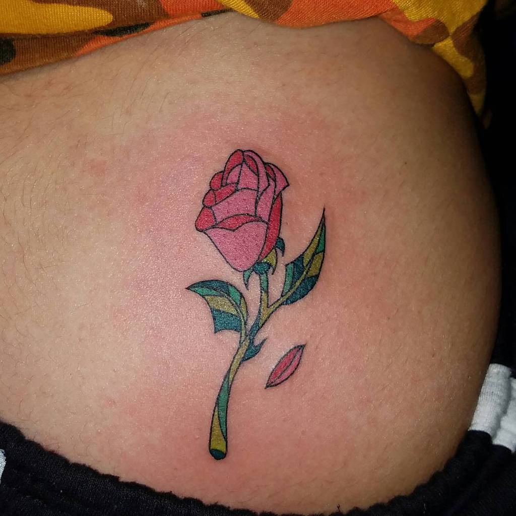 A vibrant rose tattoo on skin with one detached petal