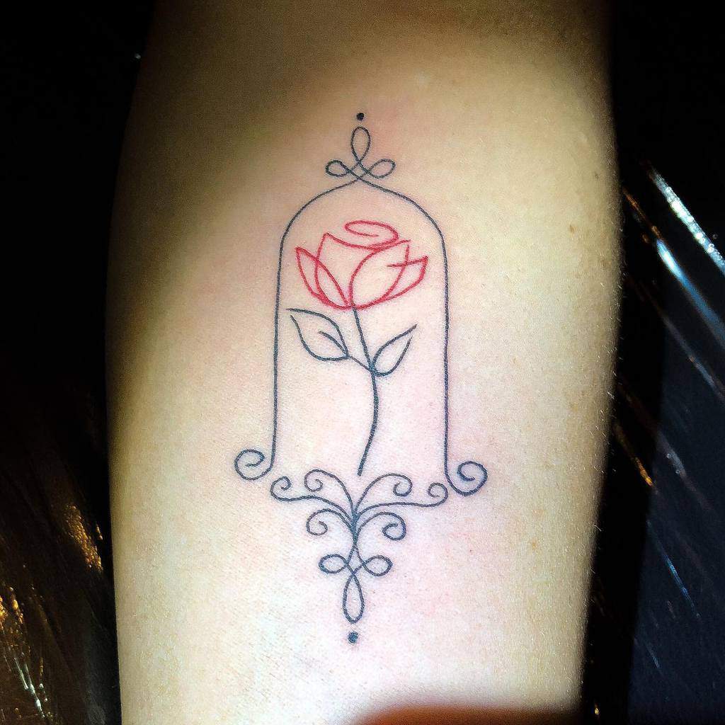 A simple, minimalist Beauty and the Beast rose tattoo inside a glass dome, with delicate lines and a touch of red for the rose