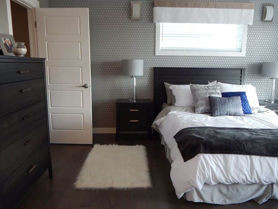 Modern bedroom with dark wood furniture, white bedding, and textured grey accent wall.