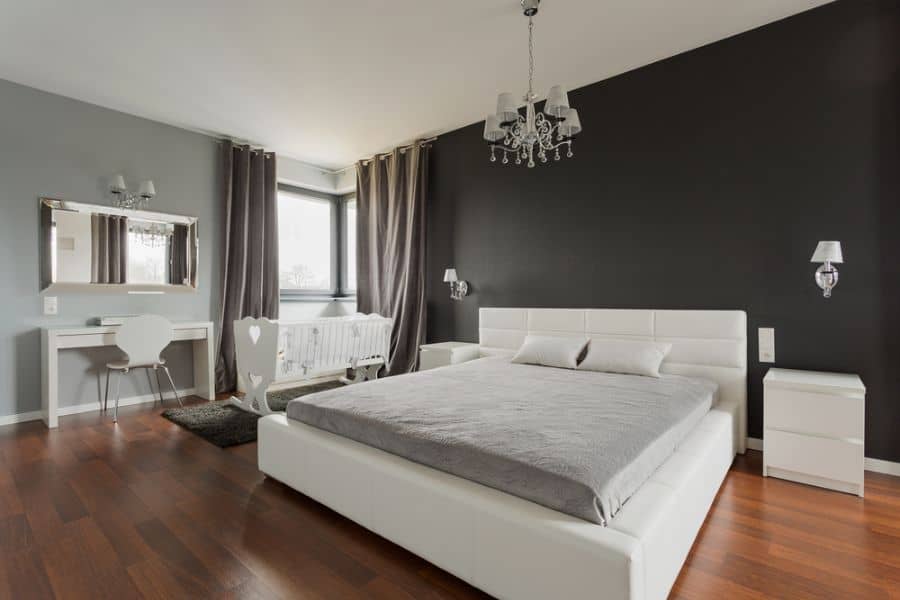 Modern bedroom with black accent wall, white furniture, grey bedding, and chandelier lighting.
