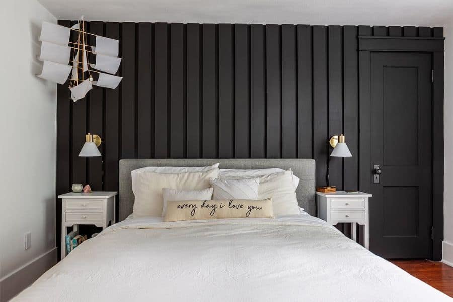 Modern bedroom with black paneled accent wall, white bedding, and gold wall sconces.