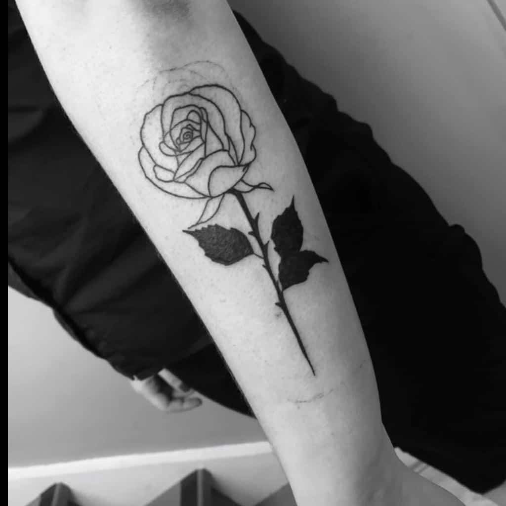 A striking black and white tattoo of a rose gracefully blooms with detailed leaves, elegantly inked on a person's forearm