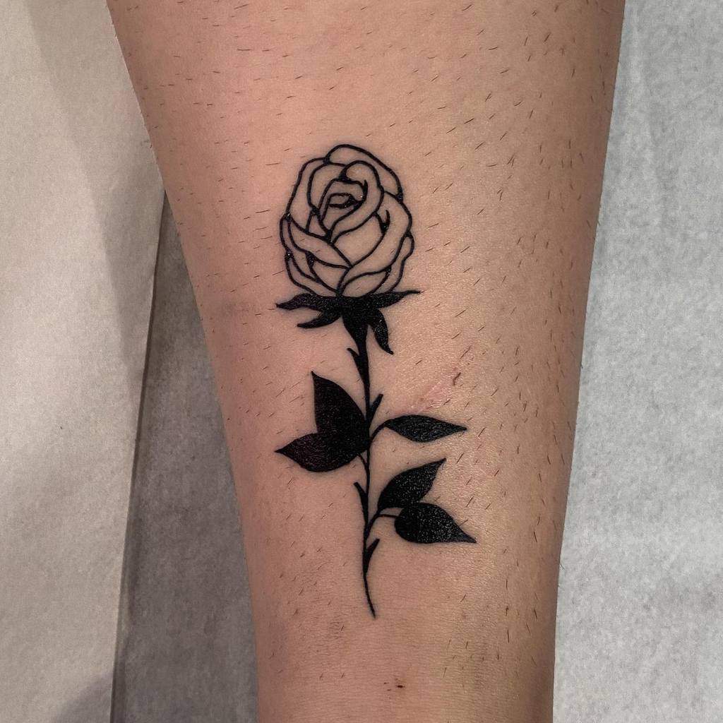 A striking black rose tattoo adorns the forearm, complete with elegantly detailed leaves and a delicate stem